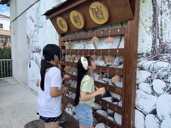 3位學生正在東新國小的校園裝置藝術東新閣掛上祝福繪馬